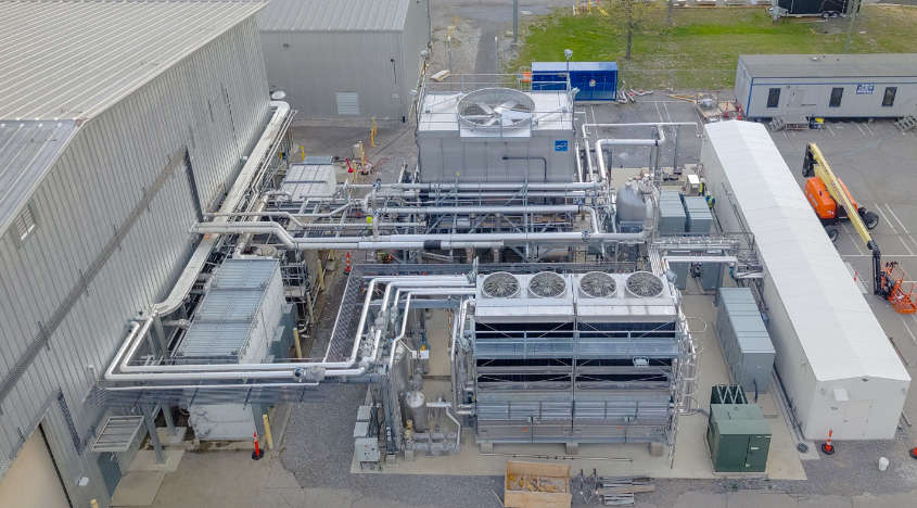 Aerial photograph showing the Material Plasma Exposure eXperiment building at Oak Ridge National Laboratory, with industrial equipment and piping surrounding the metal-roofed facility.